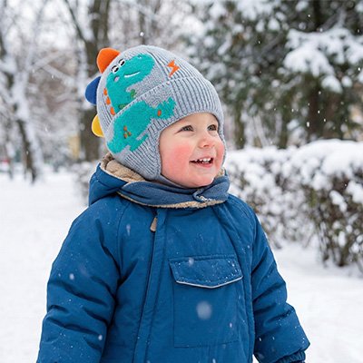Bonnet Bébé Dino bébé découvrant la neige dehors, portant un bonnet doux au toucher.