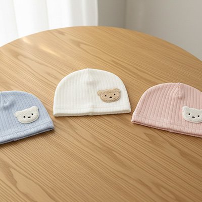 Bonnet bébé Trilli trois bonnets bébé en coton bio avec motif ourson sur une table.