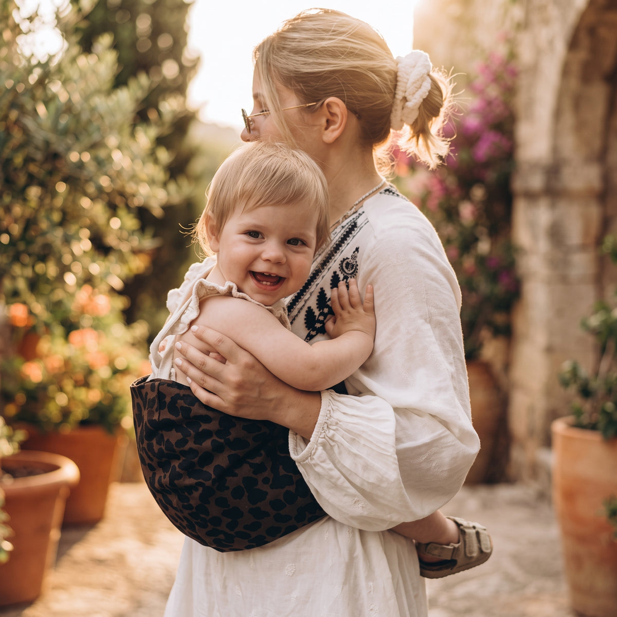 Écharpe de portage Douxora™ — bébé blotti dans l'écharpe dans un jardin de fleurs